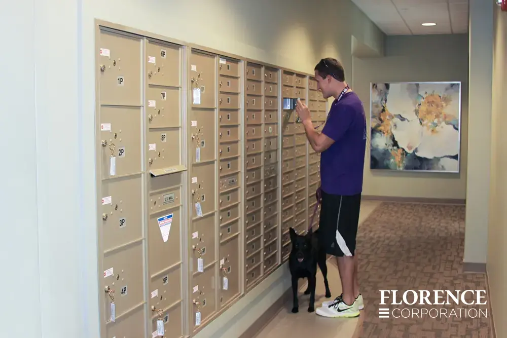 Recessed mount versatile™ 4C mailboxes and parcel lockers in sandstone with man retrieving his mail holding a leash for a black dog