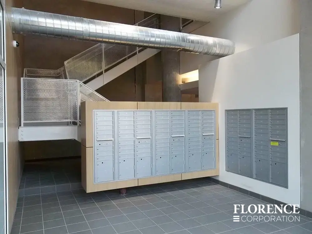 Recessed mount versatile™ 4C mailboxes in silver speck in modern area with gray tile flooring, exposed metal duct work and metal railings on stairwell