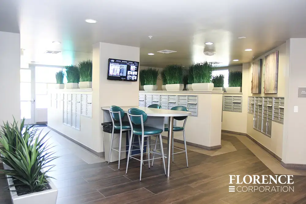 Recessed mount versatile™ 4C mailboxes in silver speck installed in multifamily apartment mailroom with green plants, green stools and wall art décor