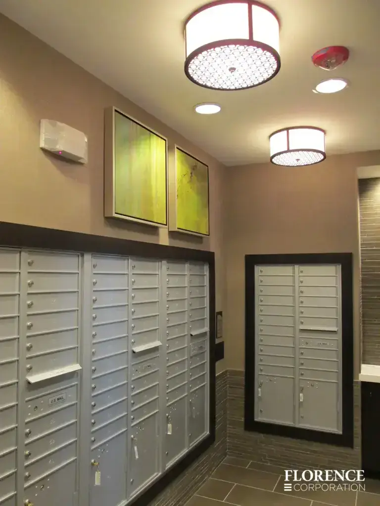 Recessed mount versatile™ 4C mailboxes in silver speck edged with black frames installed in mailroom with tan walls, tile floor, lime green art and light fixtures on ceiling
