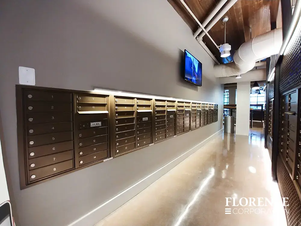 Recessed mount versatile™ 4C mailboxes in antique bronze installed in mailroom lobby area of multifamily apartment building with wooden ceiling and mounted tv