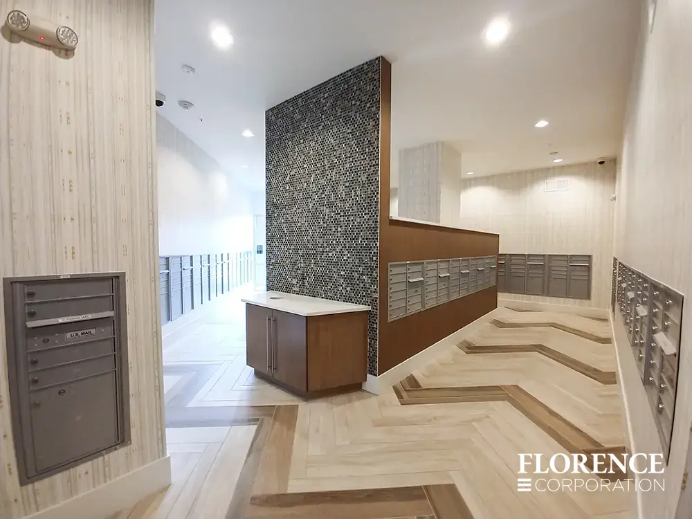 Recessed mount versatile™ 4C mailboxes in silver speck installed in large expansive residential mailroom in multifamily building with herringbone patterned tile floor and wall paper walls