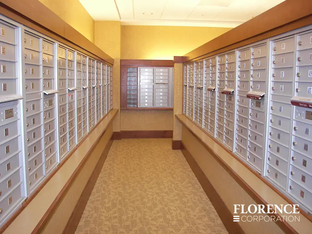 Recessed mount versatile™ 4C mailboxes in silver speck installed in multifamily apartment mailroom with wood trip and floral carpeting