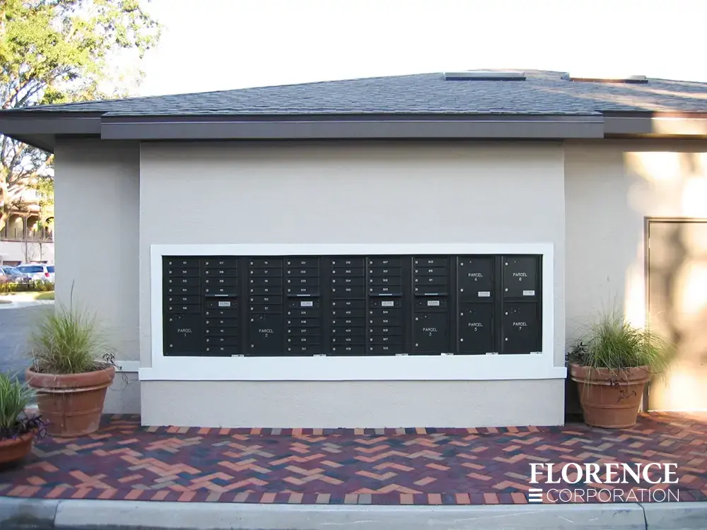 recessed mounted versatile™ 4C mailboxes and parcel lockers in black installed outdoors in wall with herringbone patterned pavers and green plants
