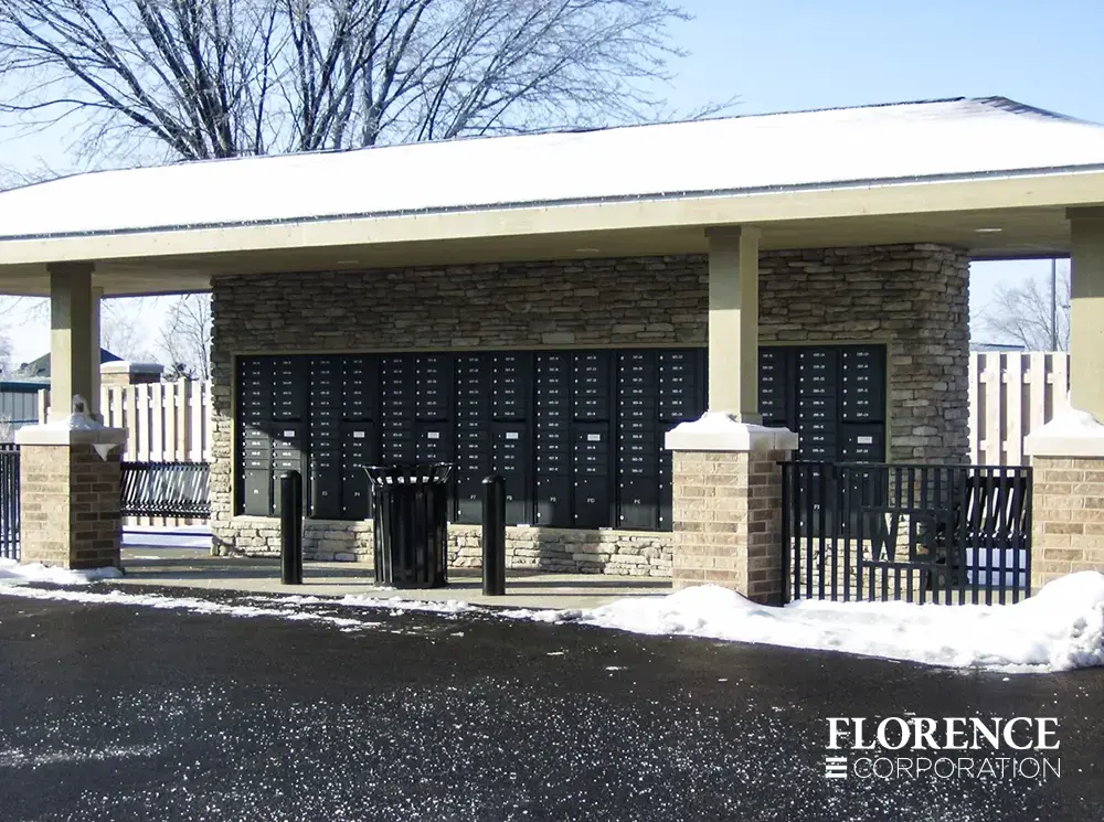 row of black recessed mounted versatile™ 4C mailboxes in stone wall under covered pavilion with black trash bins, stanchions and railing