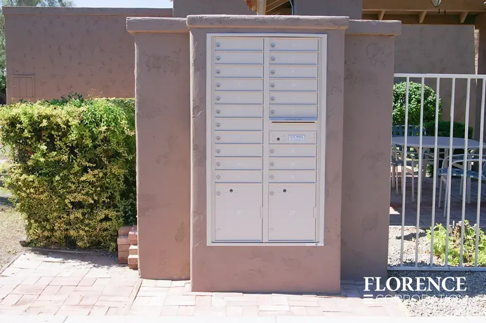silver speck recessed mounted versatile™ 4C mailboxes in pick stucco wall near white fencing and green bushes