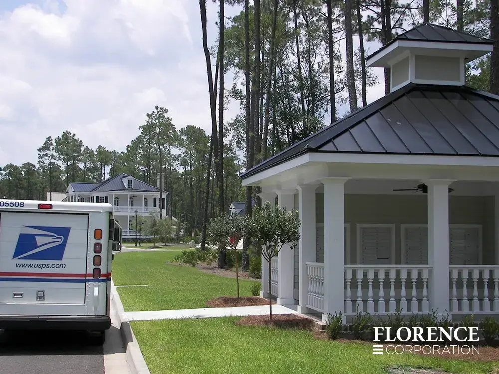 recessed mounted versatile™ 4C mailboxes in silver speck installed under covered gazebo structure near grassy area with usps delivery truck parked in the street nearby