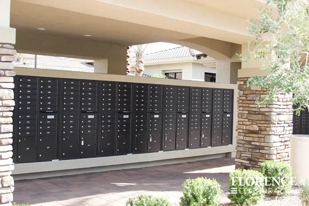 recessed mounted versatile™ 4C mailboxes in black installed in large outdoor covered mailroom with rock exterior wall and green shrubbery landscaping