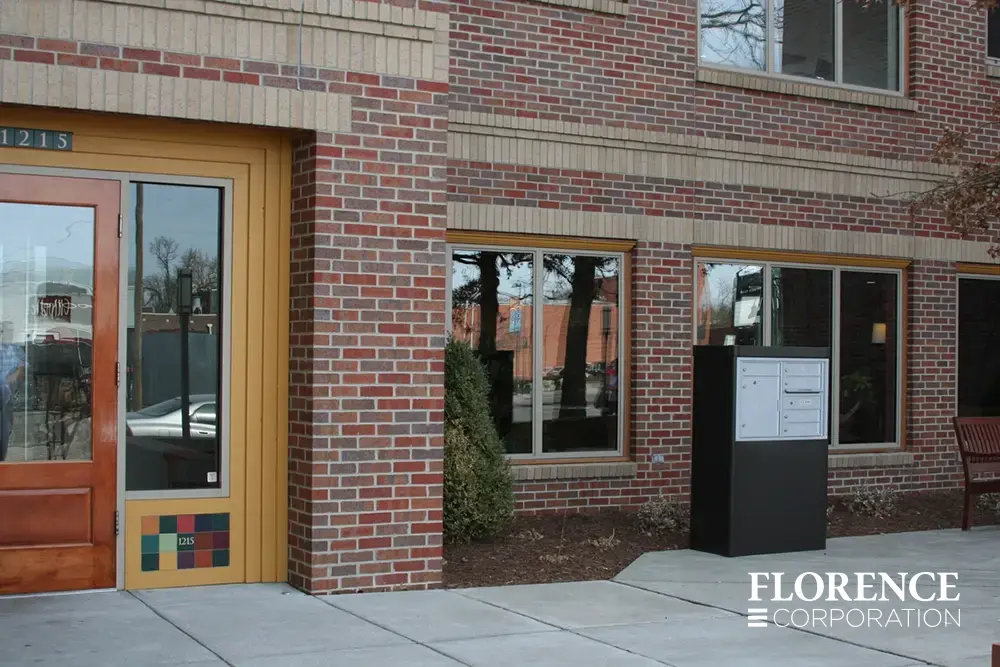 versatile™ 4C mailbox installed in dark bronze freestanding depot cabinet outdoors in front of commercial brick building space
