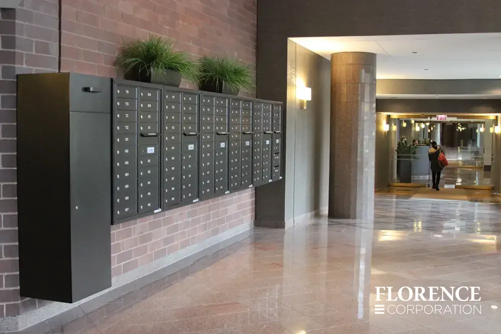 surface mounted versatile™ 4C mailboxes and large collection box all in dark bronze mounted on indoor red brick wall with decorative plants in lobby of multifamily residential building