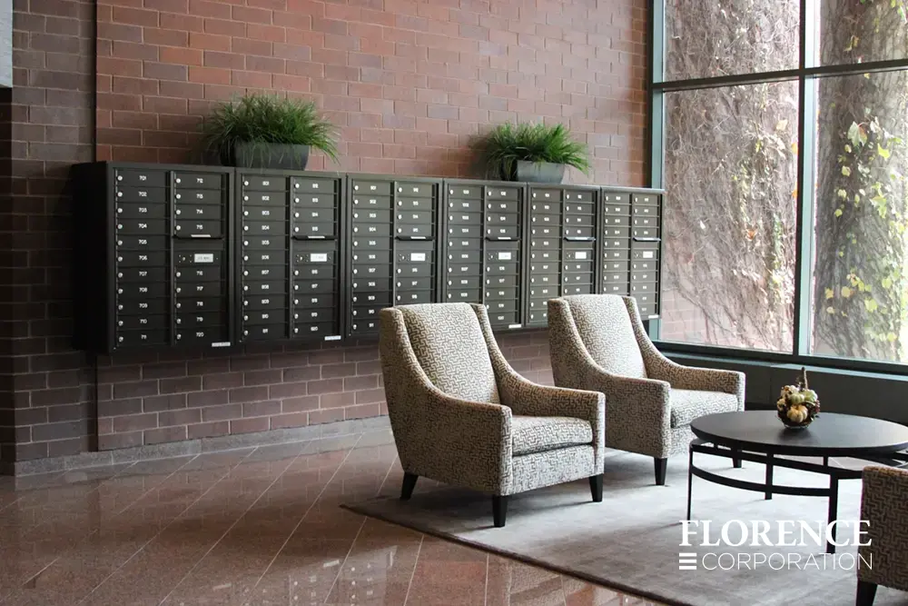 surface mounted versatile™ 4C mailboxes in dark bronze located in lobby area of modern commercial building space with chairs and table near large window