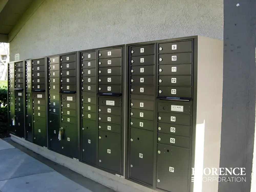 versatile™ 4C mailboxes in black mounted outdoor on side of building under weather protected cover using sandstone surface mount collars