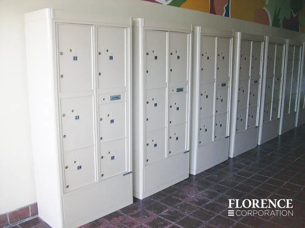 several white versatile™ 4C parcel lockers installed in white freestanding depot cabinets on red tile floor against a white wall with colorful mural above
